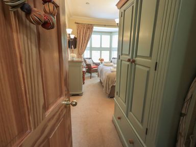 A bedroom with an open wooden door green wardrobe bed with towels and armchairs near a window covered with curtains at Heron Cottage Ambleside