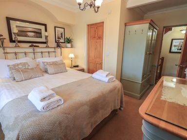 A bedroom with a bed with pillows and towels two wooden doors a wardrobe and a dresser at Heron Cottage in Ambleside