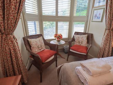 A sitting area with two wicker chairs and a small round table by windows with shutters at Heron Cottage in Ambleside