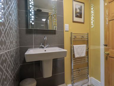A bathroom with a sink a mirror a towel rack with a towel and a wooden door at Heron Cottage in Ambleside