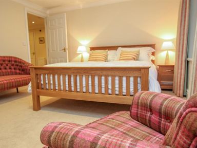 A bedroom with a wooden bed with striped pillows two lamps on wooden nightstands and plaid chairs at The Miller in Ambleside