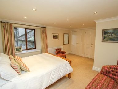 A bedroom with a bed white bedding and striped pillows a window with curtains two armchairs and framed pictures on walls at The Miller in Ambleside