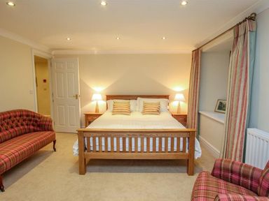 A bedroom with a wooden bed two bedside tables with lamps striped curtains and plaid upholstered chairs at The Miller in Ambleside