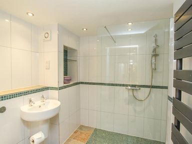 A bathroom with a wall-mounted sink a walk-in shower with glass screen and a towel radiator at The Miller in Ambleside