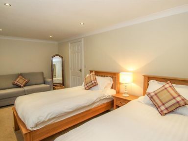 A bedroom with two wooden single beds a bedside table with a lamp a gray sofa and a standing mirror at The Miller in Ambleside