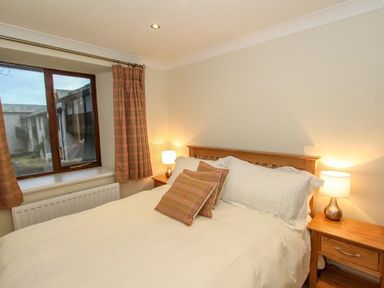 A bedroom with a wooden bed frame a bed with white bedding and plaid pillows wooden bedside tables with lamps and a window with plaid curtains at The Miller in Ambleside