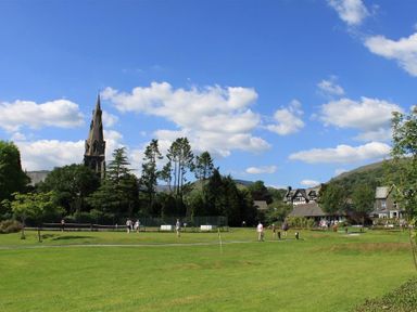 A park with people walking and playing sports near trees and buildings at The Miller in Ambleside
