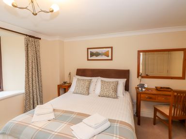 A bedroom with a neatly made bed bedside tables a desk chair and a large mirror at Waterfalls Ambleside