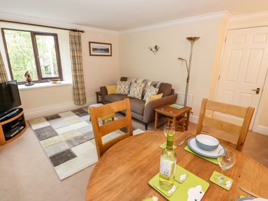 A living room with a sofa pillows a floor lamp wooden dining table set with dishes and wine bottle at Waterfalls in Ambleside