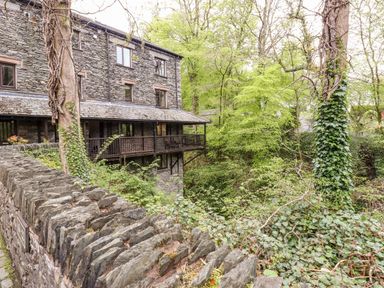 A stone house with a wooden balcony surrounded by trees and a stone wall with ivy at Waterfalls in Ambleside