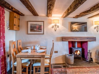 A dining area with wooden table and chairs set with dishes next to a fireplace with a wood-burning stove and wall-mounted TV at Knotts Cottage in Troutbeck