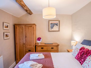 A bedroom with a wooden wardrobe and dresser a bed with pillows and folded towels at Knotts Cottage in Troutbeck