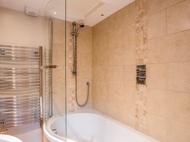 A bathroom with a bathtub shower combination stone tiled walls and a chrome towel radiator at Knotts Cottage in Troutbeck