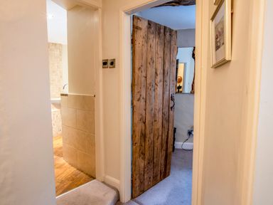 A hallway showing a wooden door opening into a carpeted room and a tiled area with wooden flooring at Knotts Cottage in Troutbeck