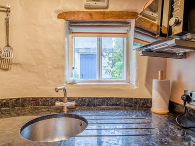 A kitchen sink with faucet a small window paper towel roll and microwave at Knotts Cottage in Troutbeck