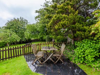 An outdoor patio with wooden table and chairs surrounded by wooden fence and green trees at Knotts Cottage in Troutbeck