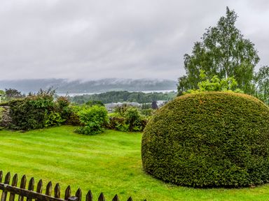 A garden with trimmed bushes and trees with a view of distant hills at Knotts Cottage in Troutbeck