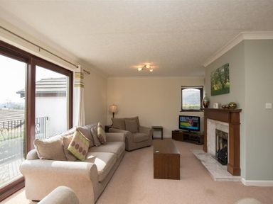 A living room with beige sofas, wooden coffee table, fireplace, television, and large window with curtains at Todd Crag in Ambleside