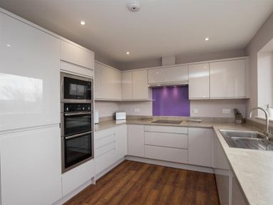 A kitchen with white cabinets a double oven a purple backsplash and a sink on a countertop at Todd Crag in Ambleside