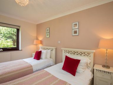 A bedroom with two single beds with red pillows two bedside tables with lamps and a window showing greenery at Todd Crag in Ambleside