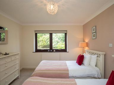 A bedroom with two single beds with pink and white bedspreads a dresser a window and a lamp at Todd Crag in Ambleside