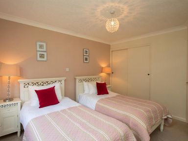 A bedroom with two single beds each with a red pillow two bedside tables with lamps and two framed pictures on the wall at Todd Crag in Ambleside