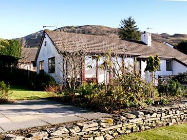 A single-story house with a tiled roof surrounded by a garden and stone wall at Todd Crag in Ambleside