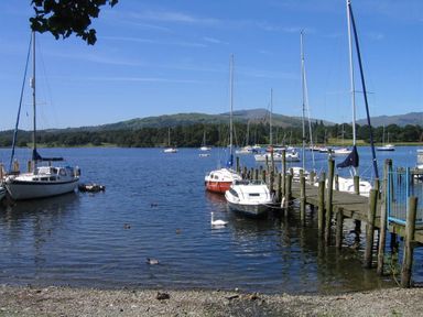 A lake with sailboats moored by a wooden dock and hills in the background at Todd Crag in Ambleside