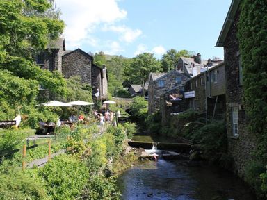 A stone building cafe next to a river with people sitting under umbrellas at Todd Crag in Ambleside
