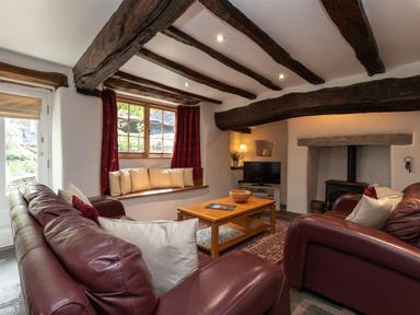 A living room with exposed wooden beams a wood burner two leather sofas a wooden coffee table and a window seat at Lowfold Cottage in Ambleside