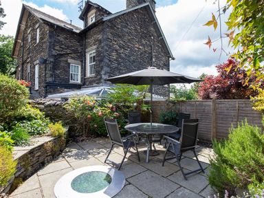 An outdoor patio area with a round table and chairs under a large umbrella next to a stone house at Lowfold Cottage in Ambleside