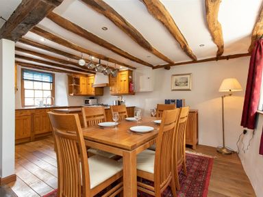 A dining area with wooden table and chairs set with plates and glasses adjacent to a kitchen with wooden cabinets and hanging pots at Lowfold Cottage in Ambleside
