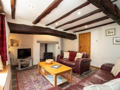 A living room with wooden beams on the ceiling leather sofas a wooden coffee table a television and a stove at Lowfold Cottage in Ambleside