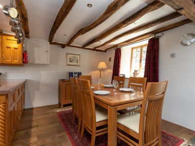 A dining area with a wooden table set with plates and glasses six wooden chairs a window with curtains and exposed wooden beams on the ceiling at Lowfold Cottage in Ambleside
