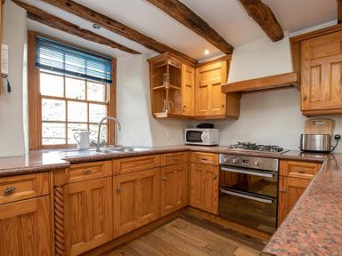 A kitchen with wooden cabinets a stove a microwave a toaster and a window with wooden blinds at Lowfold Cottage in Ambleside