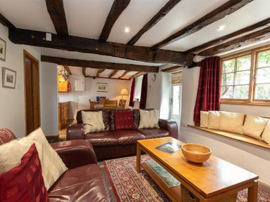 A living room with leather sofas cushions a wooden coffee table a rug and exposed wooden beams at Lowfold Cottage in Ambleside