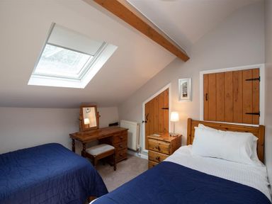 A bedroom with two single beds a wooden dresser a bedside table with a lamp and skylight window at Lowfold Cottage in Ambleside