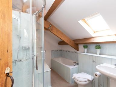 A bathroom with a glass shower, bathtub, toilet, sink, skylight, and wooden beams at Lowfold Cottage in Ambleside