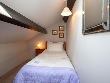 A small bedroom with a single bed a bedside table with a lamp three framed pictures on the wall and a hanging light at Lowfold Cottage Ambleside