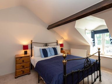 A bedroom with a metal bed frame blue bedding wooden bedside tables with lamps and a window with blue curtains at Lowfold Cottage in Ambleside