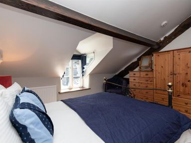 A bedroom with a bed with blue bedding a window wooden wardrobe and chest of drawers at Lowfold Cottage in Ambleside