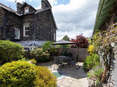A patio with a round table and chairs under an umbrella surrounded by shrubs and flowers at Lowfold Cottage in Ambleside
