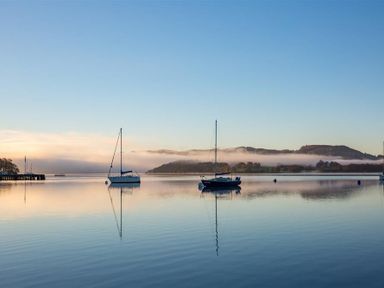 Two sailboats on calm water with hills and low fog in the background at Lowfold Cottage in Ambleside