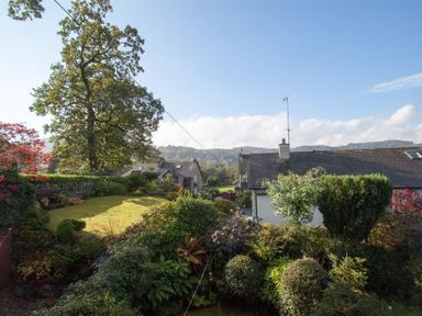 A garden with various bushes and trees near houses under a clear sky at Sunset Cottage in Ambleside