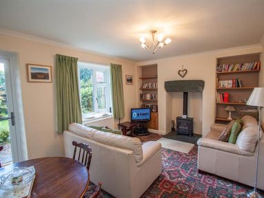 A living room with two sofas a small TV a wood stove and bookshelves at Sunset Cottage in Ambleside