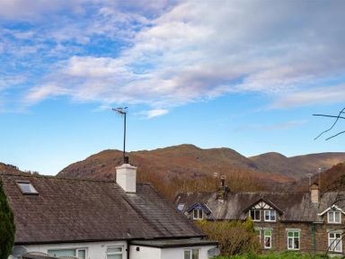 Rooftops of houses with chimneys and an antenna with hills in the background at Sunset Cottage in Ambleside