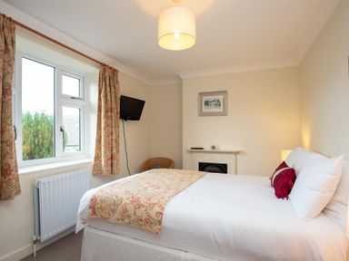 A bedroom with a bed bedside lamp wall-mounted tv curtain and window at Sunset Cottage in Ambleside