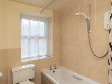 A bathroom with a bathtub a showerhead a toilet and a frosted window at Sunset Cottage in Ambleside
