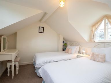 A bedroom with two single beds a side table with a lamp a dressing table and a window at Sunset Cottage in Ambleside