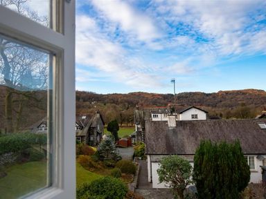 A view of houses and trees with hills in the background seen through an open window at Sunset Cottage in Ambleside